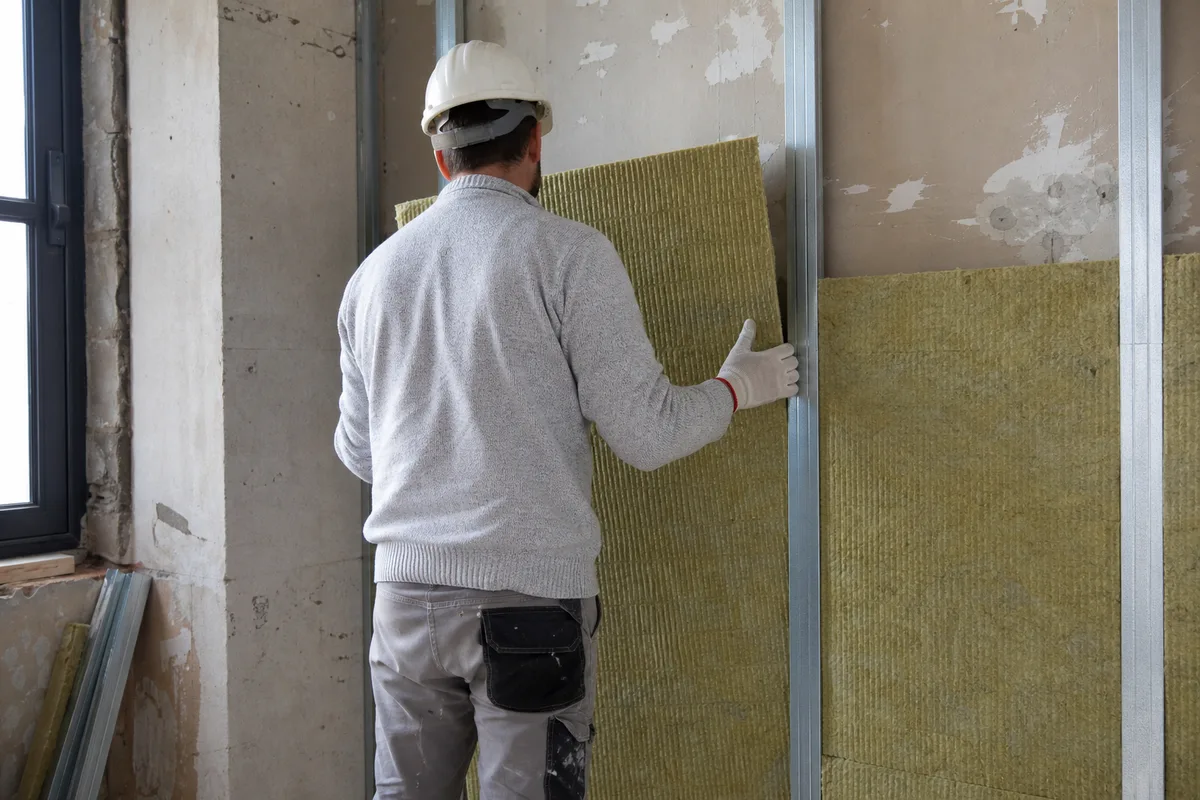 Artisan de dos posant une isolation thermique sur un mur intérieur en rénovation
